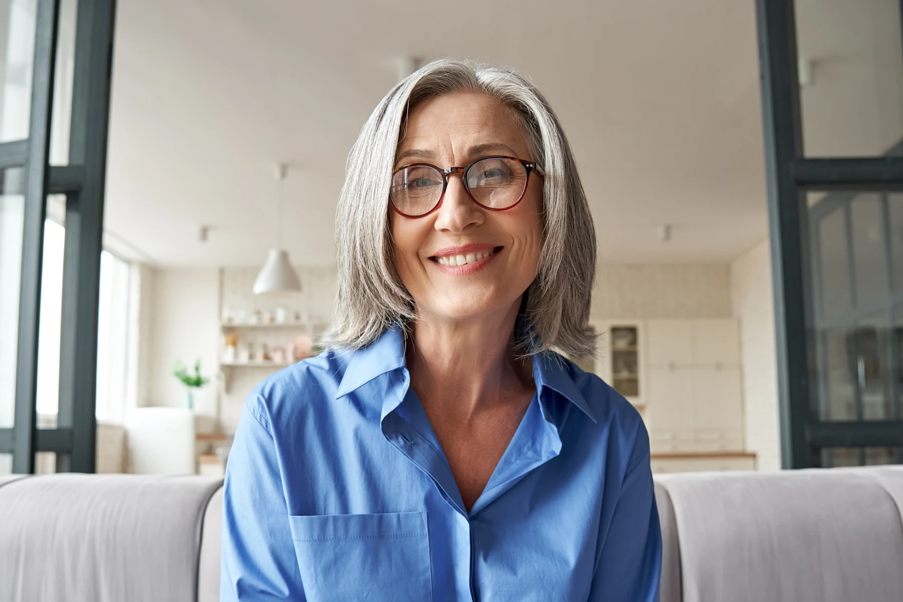 A smiling woman in a blue shirt seated in a bright room.